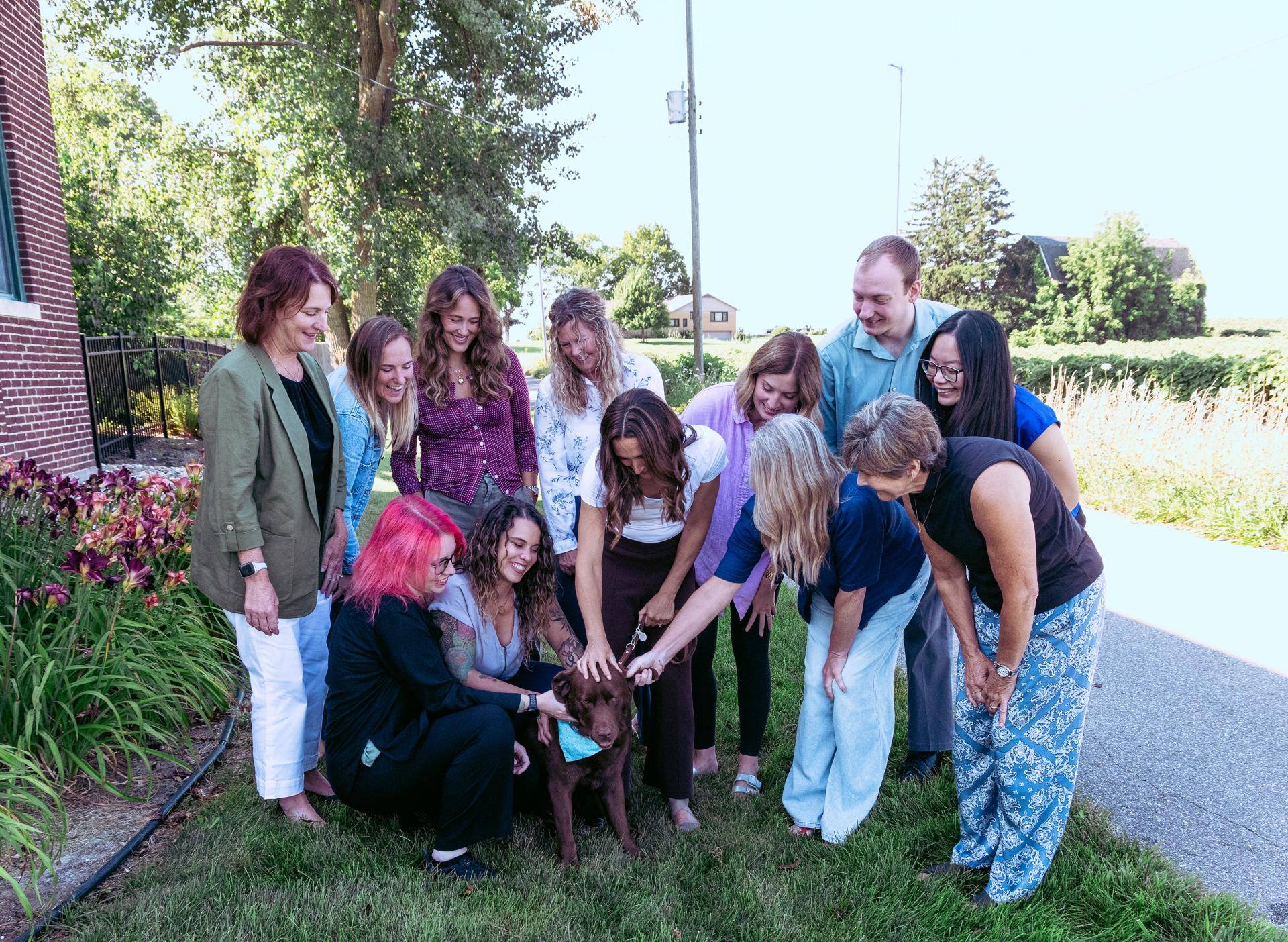 a group of adults crowded around a brown lab retriever