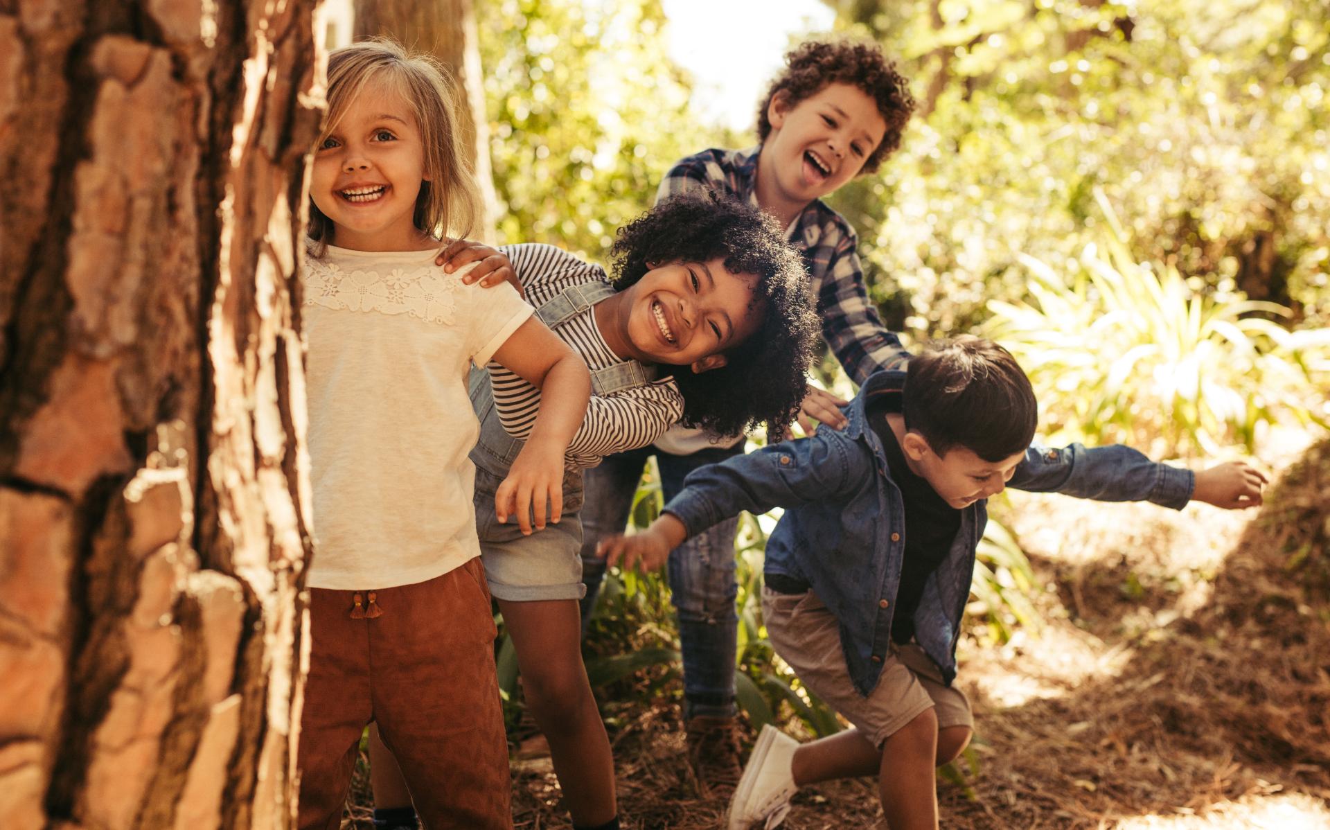 Four kids playing behind a tree in the woods