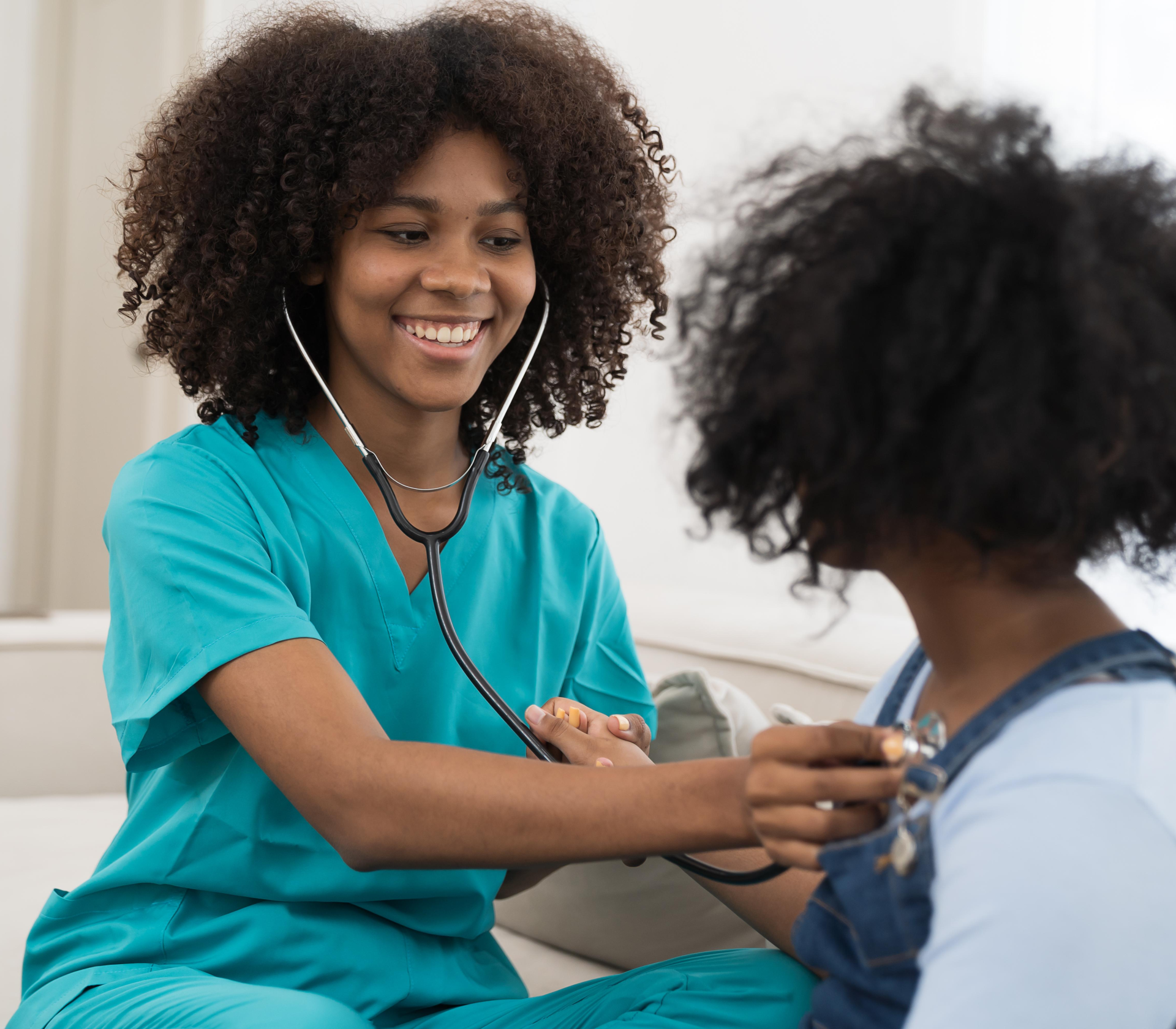 Smiling nurse in teal scrubs uses a stethoscope on a child wearing overalls. The setting is bright and cheerful, conveying care and comfort.