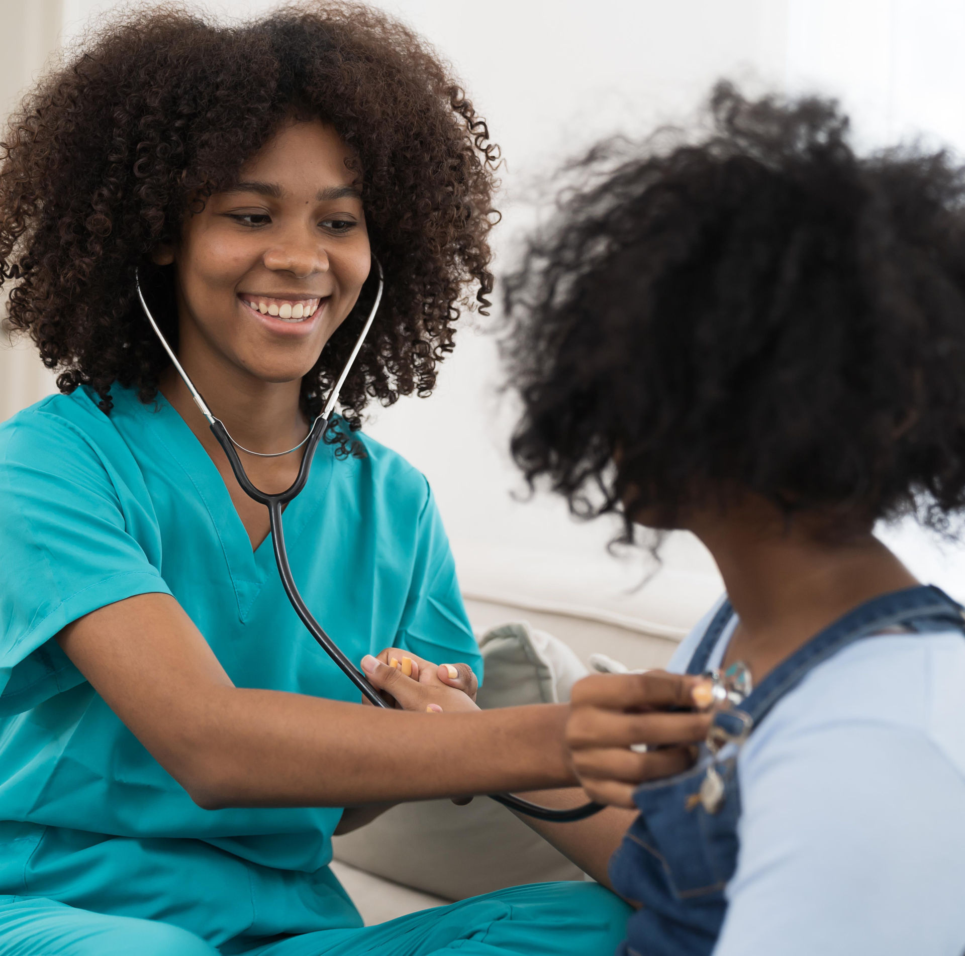Smiling nurse in teal scrubs uses a stethoscope on a child wearing overalls. The setting is bright and cheerful, conveying care and comfort.