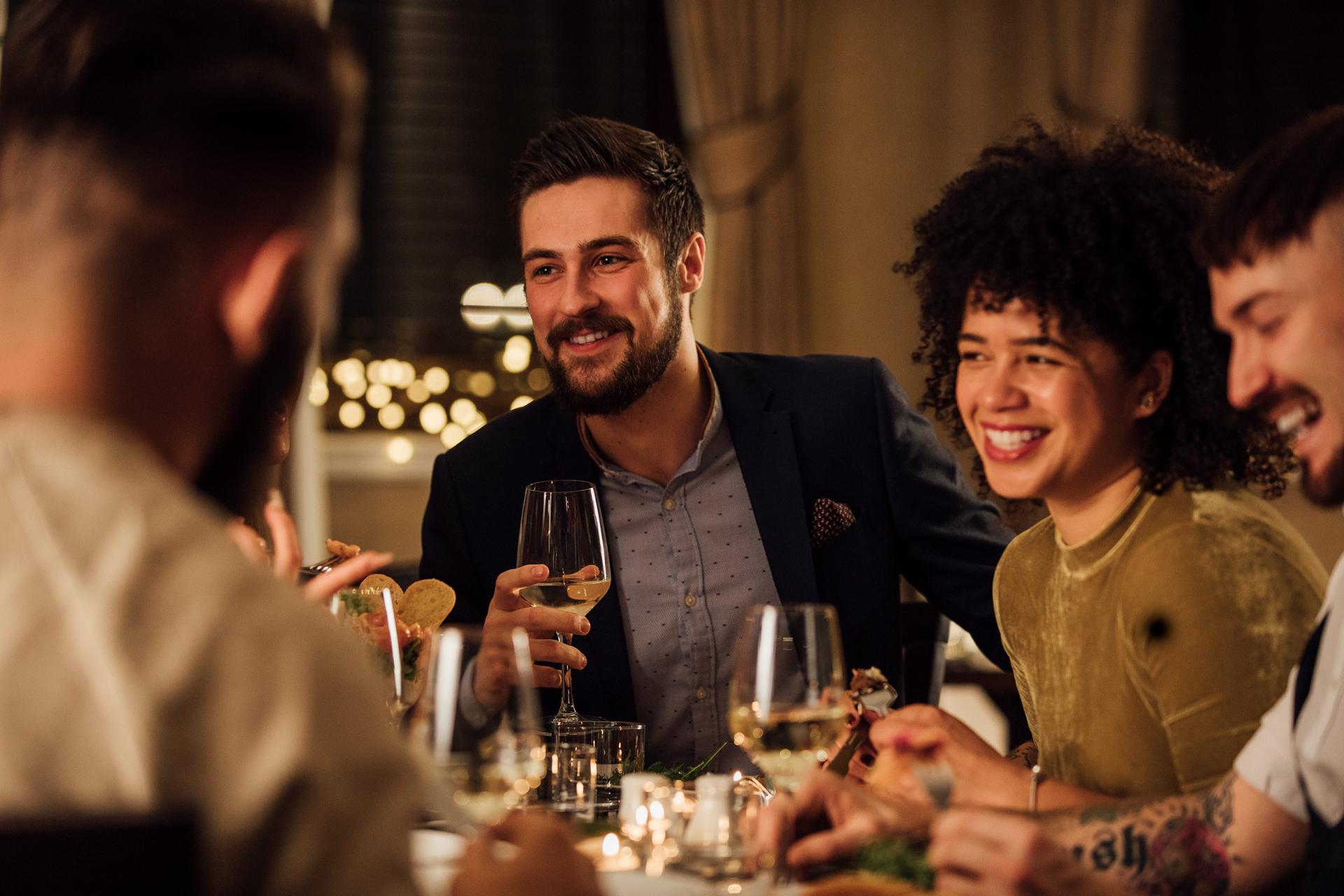 A group of friends enjoys a cozy dinner, chatting and laughing around a candle-lit table. Warm lighting and smiles create a joyful, intimate atmosphere.