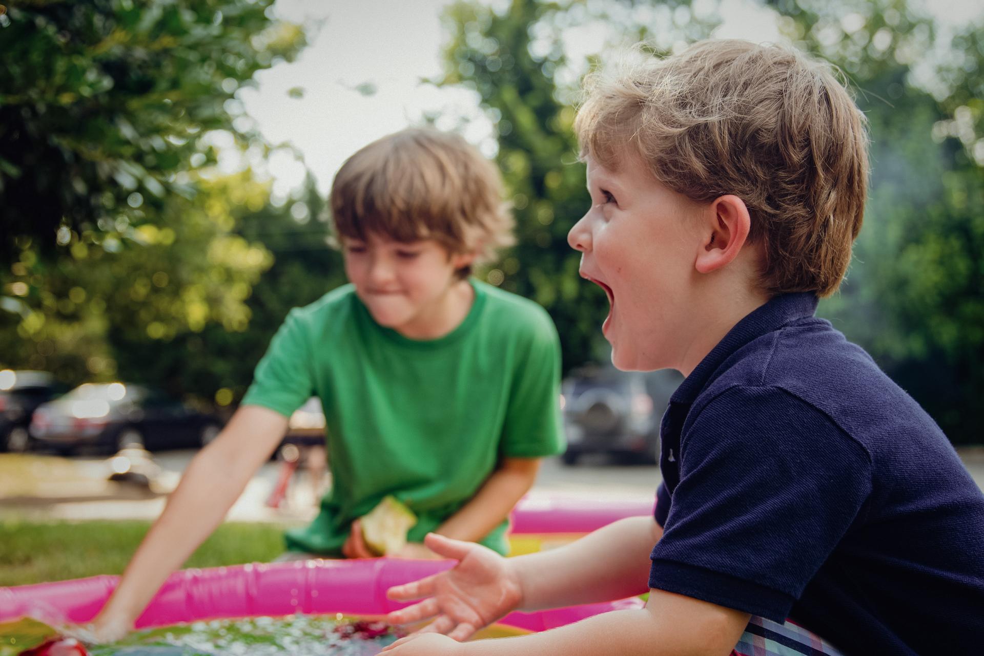 Two boys playing with an inflatable pool outdoors.